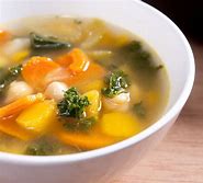 This ilmage is of a white bowl containing a vegetable soup with broccoli and carrots. It is in a thin broth