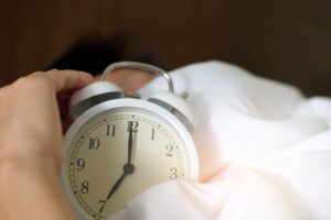 this image shows someone in bed holding an alarm clock