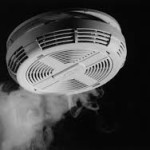a white smoke detector against a black background showing some smoke nearlby