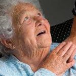 this image shows an elderly lady looking up to her carer whilst touching her hand.