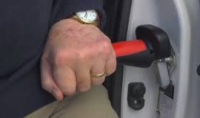 this image shows a hand on a red and black handle which is hooked into the hinge of a car.