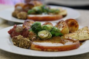Cooking for the elderly at Christmas. Image shows a plated Christmas dinner from the side on. The plate is white and holds a thick slice of turkey with gravy, brussell sprouts halved, roast potatoes and stuffing.
