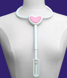 This image shows a Bra Angel gadget to help you put your bra on with one hand. It is made of white plastic and clips around your neck. It has a pale pink heart at the front and an extension to hold the strap in place