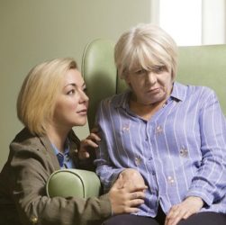 this image shows a woman sat in a large green chair who has had a stroke. Her Daughter kneels beside her