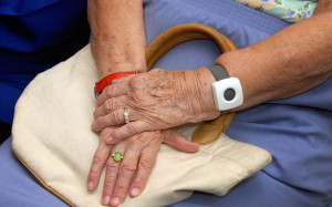 this image shows someone elderly with their hands in their lap and wearing a call bell on one wrist