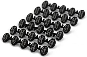 Image shows Attach-a-tag laundry labels for care homes. They are black plastic disks showing the name Geoff Harris for demonstration purposes. The tags are on a plastic strip.