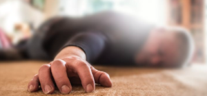 How To Prevent A Fall At Home. This image is blurred for effect but it shows an older person laying on the floor after a fall. His arm is in the foreground and you can clearly see his hand. His head and body are blurred but he is wearing a dark coloured top.