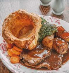 Good diet for elderly people. This image shows a large yorkshire pudding, sliced roast beef, broccoli, sliced carrots and gravy.
