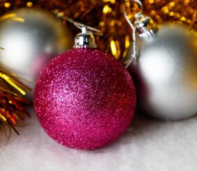 This image shows two silver Christmas baubles and one pink bauble resting in some gold tinsel