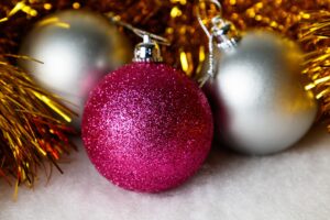 This image shows two silver Christmas baubles and one pink bauble resting in some gold tinsel