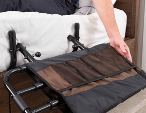 How to stop someone falling out of bed. This image shows a brown and black bed rail that folds down. It is fixed in place under the mattress itself.