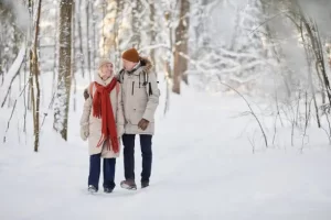 Financial help this Winter. This image shows an elderly couple walking in a wood. There is heavy snow on the ground and on the trees. They are wrapped up against the cold and the woman is wearing a bright red knitted scarf. They both have hats on.