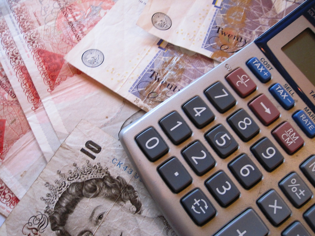 This post is about Carers allowance.This image shows English ten and twenty pound notes and a calculator