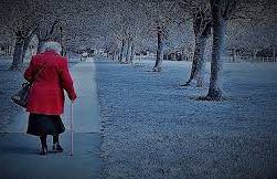 this image shows an elderly lady in a red coat walking with a stick through the park