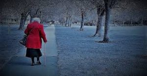 this image shows an elderly lady in a red coat walking with a stick through the park