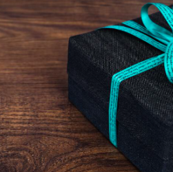 Gifts for elderly people. This image shows a dark coloured rectangular box with a turquoise ribbon tied in a bow. The gift is resting on a dark wood table.