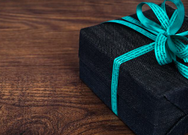 Gifts for elderly people. This image shows a dark coloured rectangular box with a turquoise ribbon tied in a bow. The gift is resting on a dark wood table.