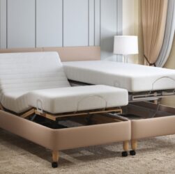 This image shows an adjustable bed. The frame has a light brown fabric covering and there are two separate mattresses on it. One is raised horizontally, the other the head and foot are raised