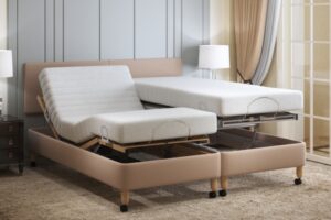 This image shows an adjustable bed. The frame has a light brown fabric covering and there are two separate mattresses on it. One is raised horizontally, the other the head and foot are raised