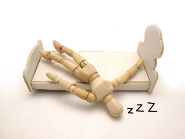 How to stop someone falling out of bed. This image shows an artists model, the wooden type, falling out of a bed. It has z's added to show the person is asleep.