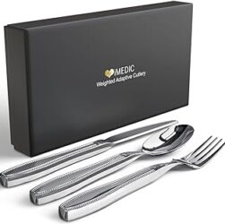 Cutlery for shaky hands. This image shows a stylish knife, fork and spoon set in stainless steel. The cutlery is arranged on a white surface and there is a black cardboard gift box behind them.