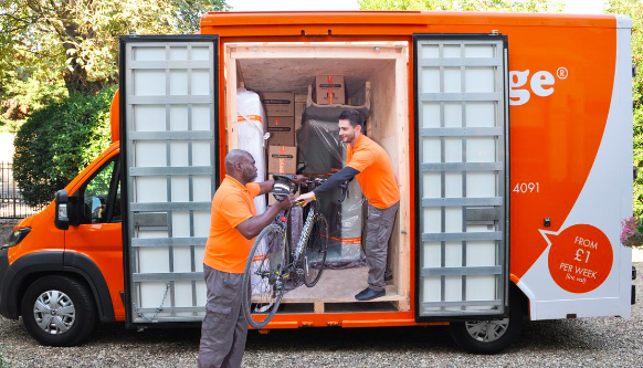 This image shows an Easy Storage team. Their are two men loading a bike onto a van via the double side doors. The van is orange and white